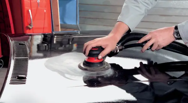 Mani esperte utilizzano una levigatrice per stuccare auto, preparando la carrozzeria per una finitura impeccabile.