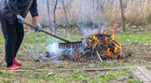 Osoba w rękawiczkach grabi ognisko na posesji, z którego unosi się dym i płomienie.