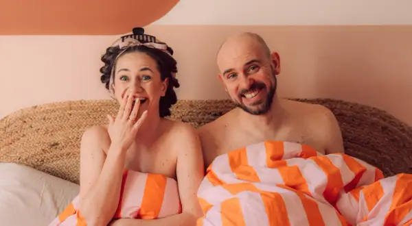 Para, uśmiechnięta, w pościeli, przygotowuje się do rozmowy o seksie.