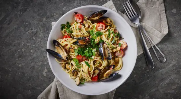 En skål med spaghetti vongole, toppad med färska örter och körsbärstomater. En klassisk italiensk rätt som passar perfekt för en mysig middag.
