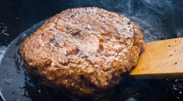 Jugosa carne dorándose en sartén, parte de como hacer hamburguesas caseras. Humo y burbujas de grasa.