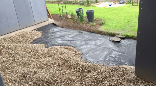 Baustelle für eine splitt terrasse mit Vlies und Kies. Im Hintergrund Rasen und Spielzeug.