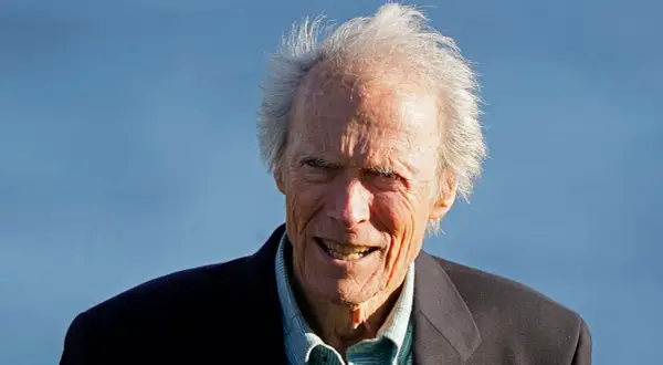 Clint Eastwood heute, mit seinem charakteristischen Lächeln und zerzaust grauem Haar, blickt in die Kamera.