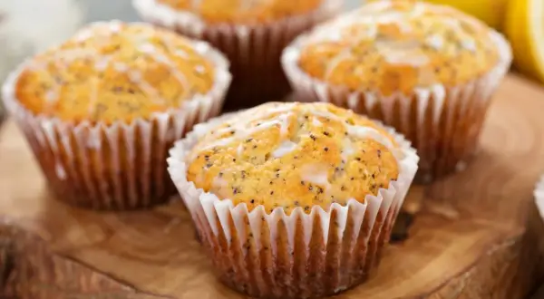 Cztery muffinki cytrynowe na oleju, posypane makiem i polane lukrem, prezentują się apetycznie na drewnianej desce.