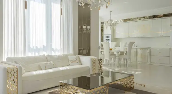 Elegancki salon i kuchnia w stylu glamour, z białymi meblami, złotymi zdobieniami i kryształowym żyrandolem.