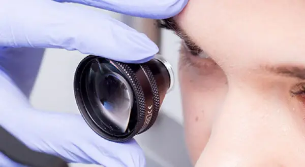 Lekarz w rękawiczce bada oko pacjenta, co może być częścią diagnostyki lub leczenia retinopatii cukrzycowej.