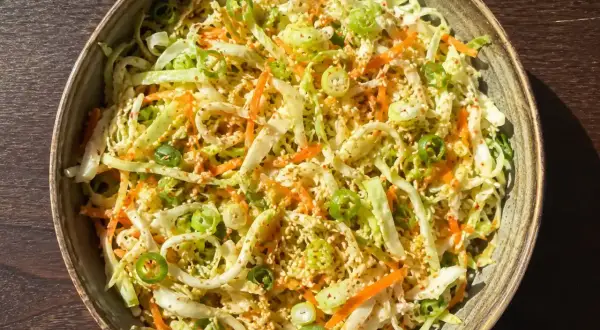 En skål med kålsallad vitkål, morötter och salladslök, toppad med sesamfrön.