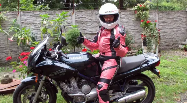 Niska dziewczyna w różowym kombinezonie motocyklowym i kasku siedzi na czarnym motocyklu Yamaha Diversion.