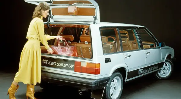 En kvinna i gul klänning lastar en väska i en silverfärgad Volvo concept car från 80-talet.