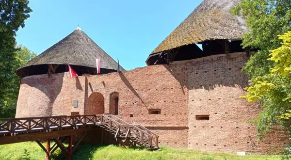 Zamek w Międzyrzeczu, ceglane mury i stożkowe dachy wież. Drewniany most prowadzi do bramy.