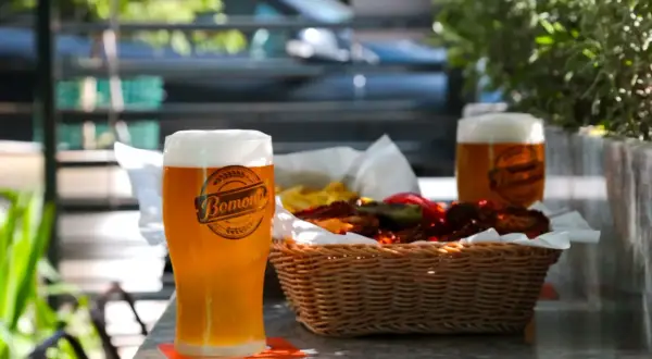 Orzeźwiające weizen piwo z pianką, obok koszyk z przekąskami i drugie piwo.
