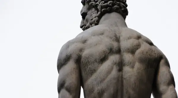 Dos des dieux Zeus, sculpture d'un homme musclé vu de dos, le ciel blanc en arrière-plan.