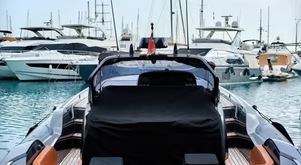 Un porto pieno di yacht di lusso, pronti per il trasporto barche. La vista è dal retro di un gommone con sedili in pelle arancione.