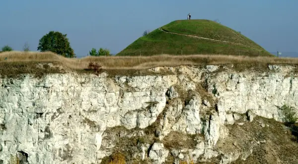 Krakus mound, zielona kopuła z dwiema postaciami na szczycie, góruje nad wapiennym klifem.