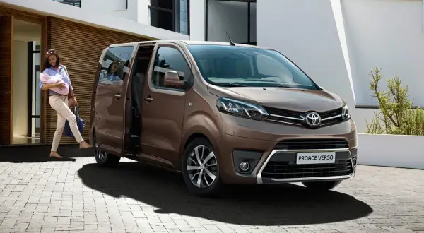 Kobieta z dzieckiem na rękach wsiada do brązowego toyoty van Proace Verso.