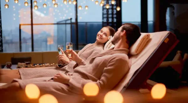 Para relaksująca w spa: para w szlafrokach z kieliszkami szampana, przy świecach.