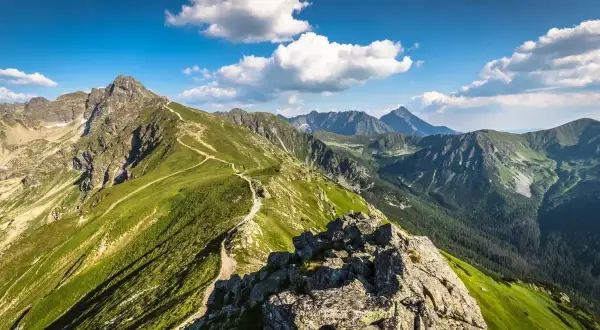 Widok na szlak prowadzący na Kasprowy Wierch. Zielone zbocza Tatr, skaliste szczyty i błękitne niebo z chmurami.