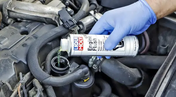 Ręka w niebieskiej rękawiczce wlewa płyn do płukania silnika Liqui Moly. Wiele osób szuka opinii o Ceratec, ale to właśnie ten produkt dba o czystość silnika.