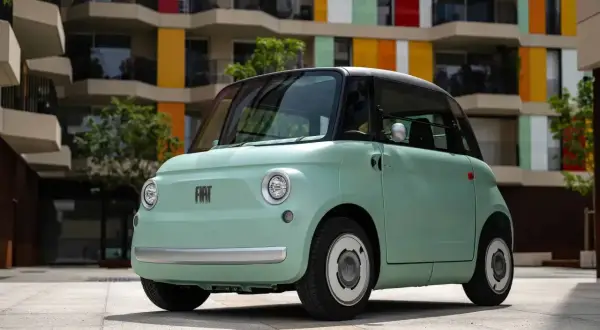 Uroczy, miętowy Fiat Topolino stoi przed kolorowym budynkiem.
