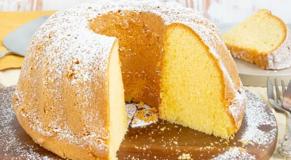 Ein saftiger vanille kuchen, bestäubt mit Puderzucker, wartet darauf, angeschnitten zu werden. Ein Stück ist bereits auf einem Teller angerichtet.