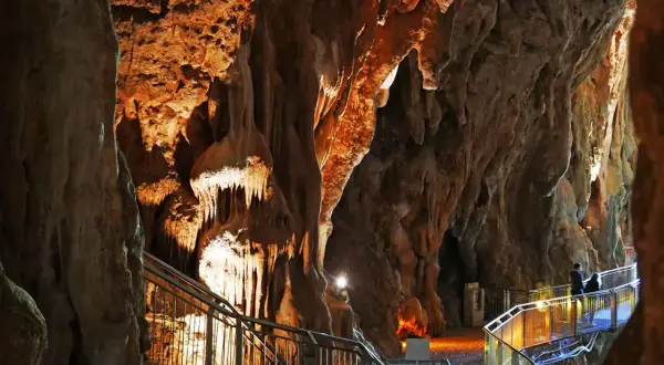 Sentiero illuminato tra le stalattiti delle grotte di Pastena, con persone che passeggiano.