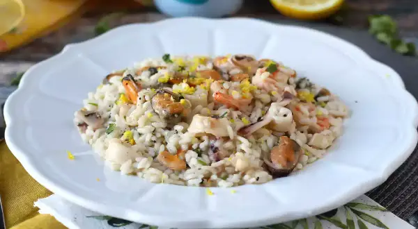 Delicioso risotto de marisco con mejillones, gambas y calamares, adornado con ralladura de limón y perejil fresco.