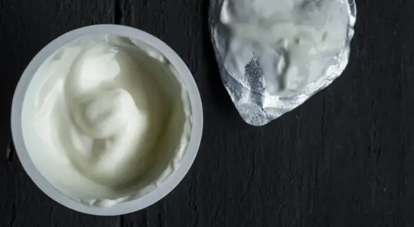 Gęsty, biały jogurt w kubeczku, obok srebrna folia. To skyr, islandzki przysmak bogaty w białko.
