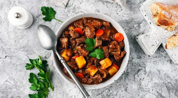 En mustig boeuf bourguignon med möra köttbitar, potatis och morötter i en rik vinbaserad sås. Serveras med en skiva rustikt bröd.