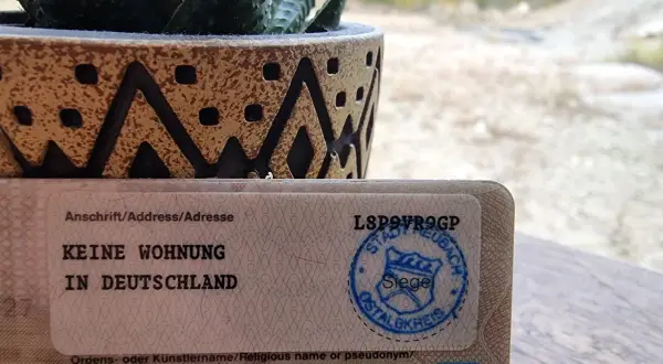 Dokument mit "Keine Wohnung in Deutschland" und einem Stempel. Ein Sukkulent in einem Topf steht daneben. So kann man dauerhaft reisend melden.