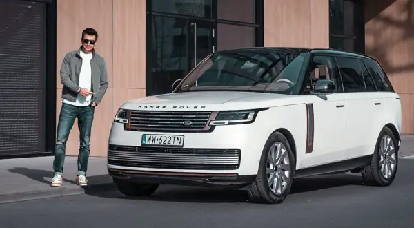 Elegancki mężczyzna w okularach stoi obok białego Range Rover 2025 z czarnym dachem.