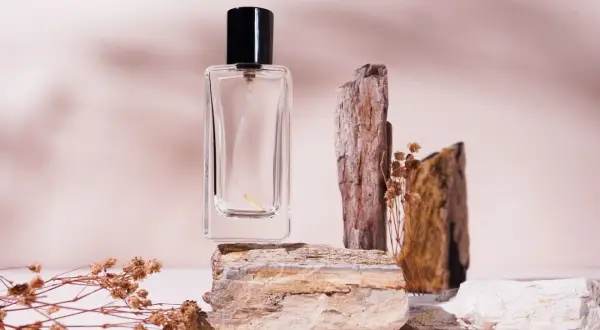 Szklana buteleczka perfum na kamieniach, otoczona suchymi gałązkami. Zapach niczym mocno pudrowe perfumy, delikatny i subtelny.