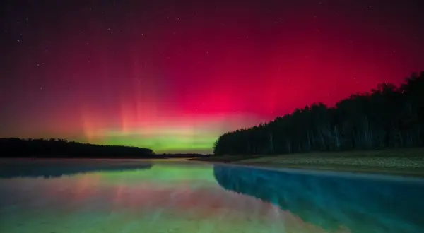 Vibrant pink and green aurora borealis reflected in a calm lake. This scene captures the magic of how to take pictures of northern lights.