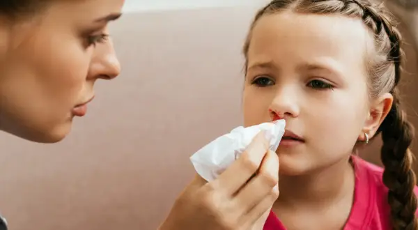 Mama delikatnie przykłada chusteczkę do nosa córki, która ma krew z nosa.