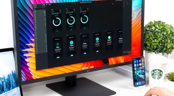 Na monitorze widać projekt aplikacji mobilnej, a obok leży laptop z otwartą **matrycą w laptopie**.