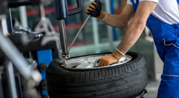 Mechanik w niebieskim kombinezonie pracuje przy montażownicy, przygotowując oponę do montażu. To ważny etap, aby sprawdzić, czy system TPMS działa poprawnie.