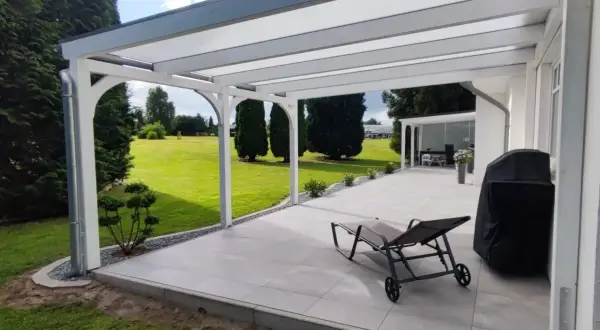 Modernes Terrassendach bauen: Ein Liegestuhl und Grill warten auf sonnige Tage unter dem neuen Dach. Der Garten lädt zum Entspannen ein.
