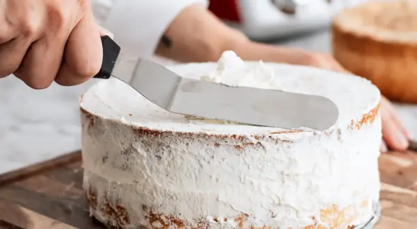 En hand sprider fluffig grädde på en tårta. Ett perfekt tårta recept att följa!