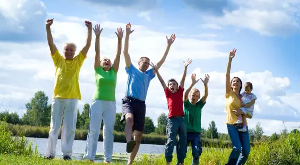 Familia disfrutando de actividades al aire libre, saltando y riendo junto a un lago.