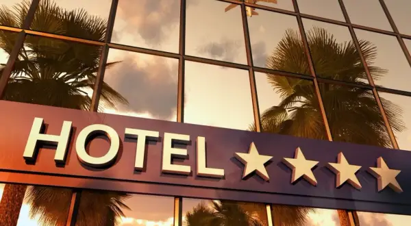 Hotel z czterema gwiazdkami, odbijający palmy i samolot w zachodzącym słońcu.