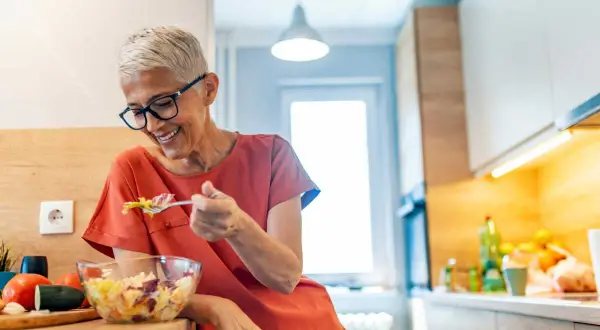 Femme souriante de 50 ans savoure une salade fraîche. Une alimentation saine pour maîtriser les calories.