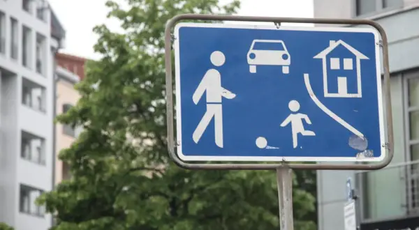 Zeichen 325.1: Fußgängerzone mit spielenden Kindern und Autos. Ein Haus symbolisiert Wohngebiet.