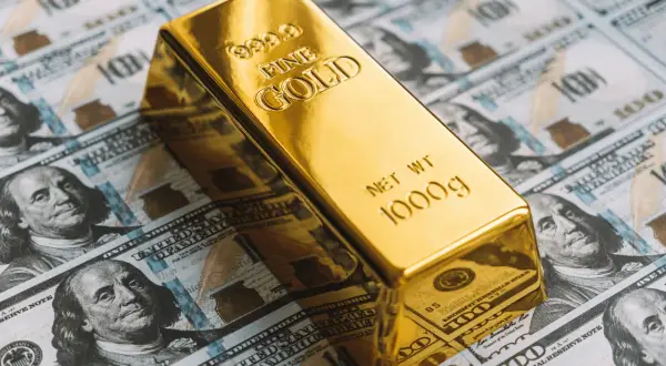 Lingote de oro de 1000g sobre billetes de cien dólares. ¿Cuánto vale 1 kg de oro?