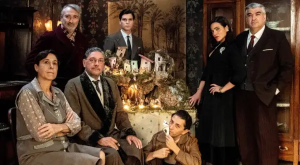 Il cast del film "Natale in casa Cupiello" posa davanti a un presepe illuminato.