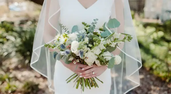 Panna młoda trzyma bukiet ślubny, w którym zastosowano technikę watowania we florystyce. Kwiaty są ułożone w luźny, naturalny sposób.