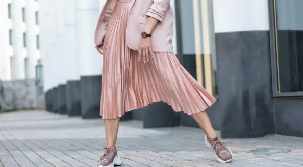 Kobieca stylizacja: pudrowy różowy żakiet i plisowana spódnica. Jakie buty do plisowanej spódnicy? Sneakersy w tym samym kolorze to strzał w dziesiątkę!