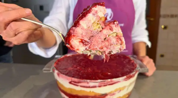 Un cucchiaio solleva una porzione generosa di tiramisù alle fragole, mostrando strati cremosi e succosi.