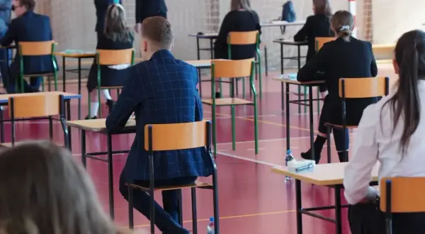 Uczniowie siedzą przy ławkach w sali gimnastycznej podczas egzaminu.