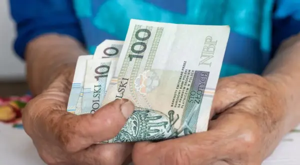 Dłonie trzymają polskie banknoty 100 zł. Czekamy na informacje, kiedy będzie wypłacana trzynastka.