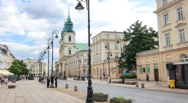 Spacer po Krakowskim Przedmieściu w Warszawie, z zabytkowymi kamienicami i kościołem w tle.