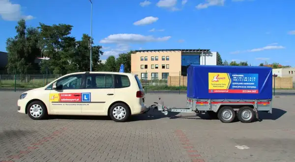 Nauka jazdy z przyczepą kempingową. Jasny samochód z literą "L" i niebieska przyczepa z logo szkoły jazdy "Expert".